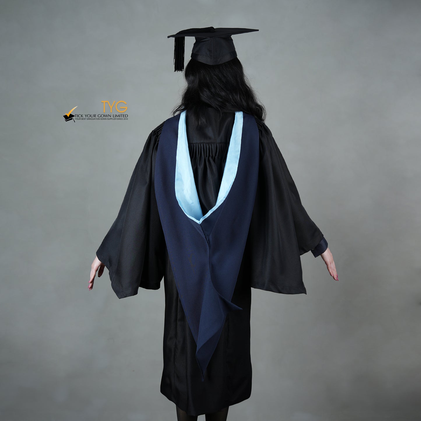 A back view of a graduate in a black cap and gown with a navy blue hood with light blue lining against a gray background