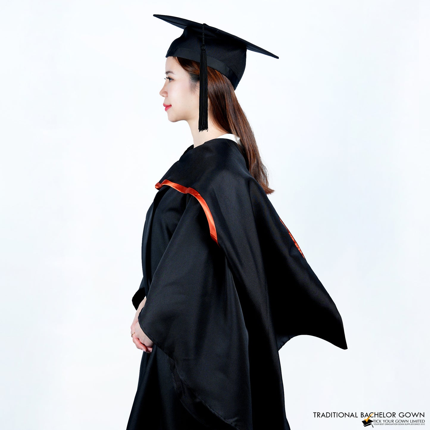 A person wearing a black bachelor graduation gown viewed from the side with a highlighted satin hood, and a mortarboard