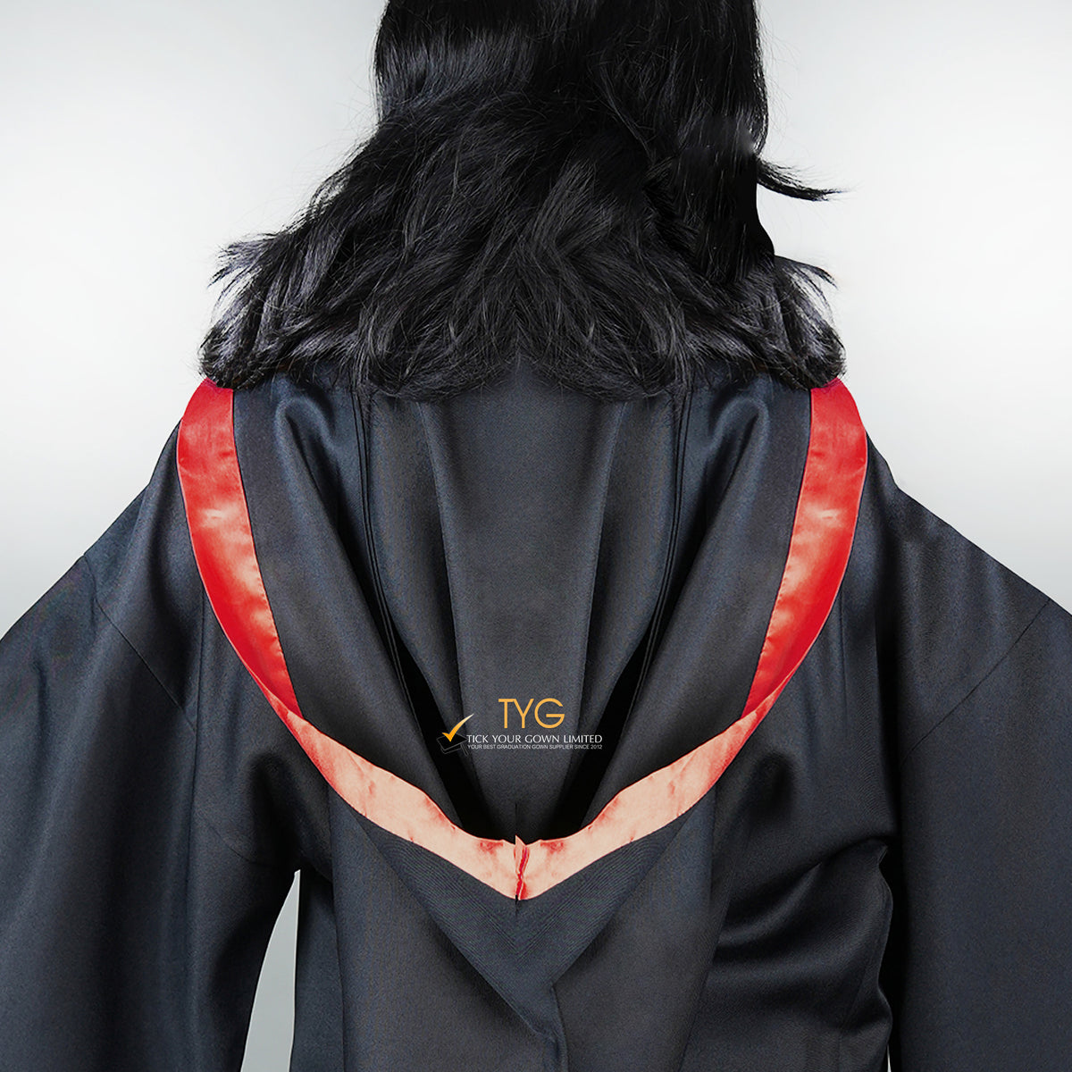 Detailed back view of a graduate in black graduation gown with a red bachelor hood against a plain background