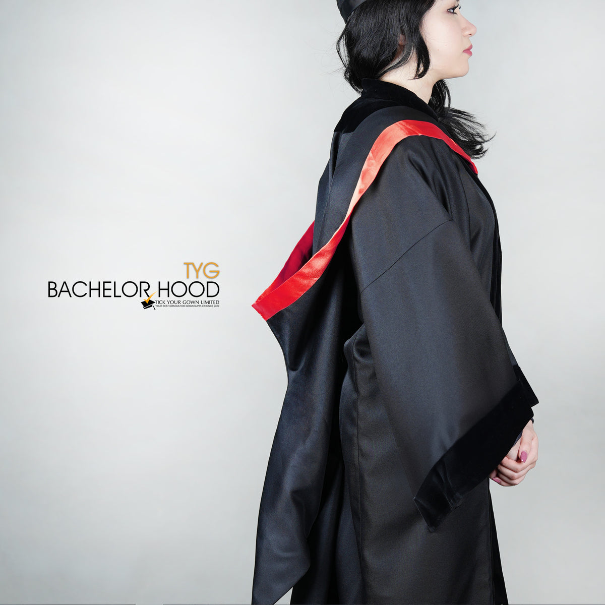 A side view of a graduate in a black graduation gown with a red bachelor hood against a plain background