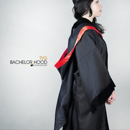 A side view of a graduate in a black graduation gown with a red bachelor hood against a plain background