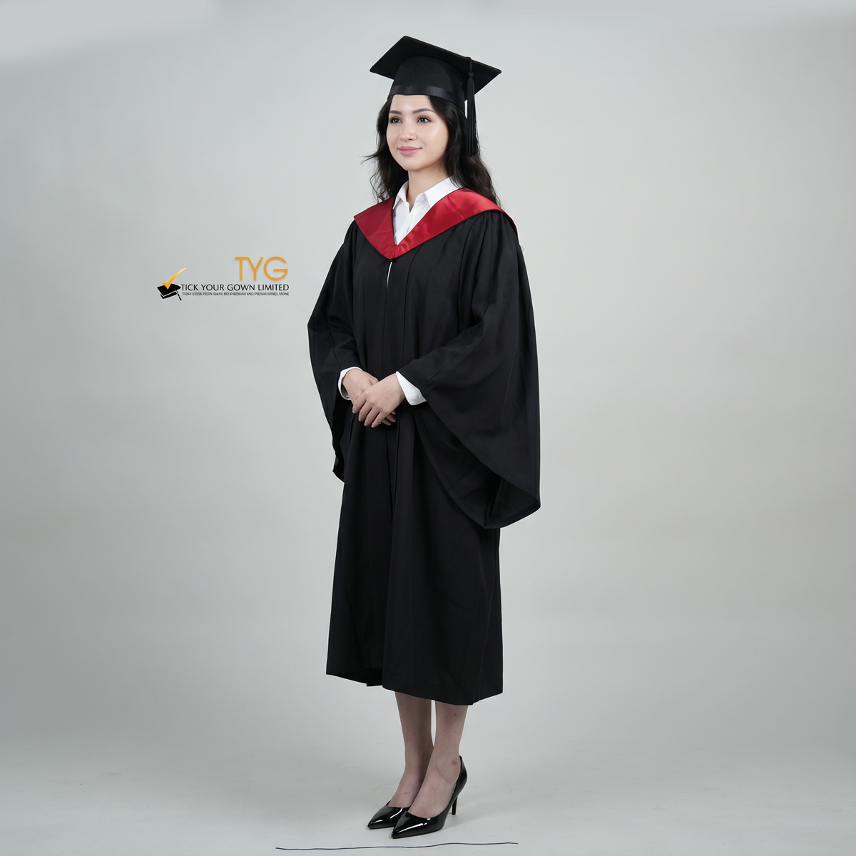 A profile view woman wearing a University of Edinburgh bachelor graduation gown and a black mortarboard cap stands against a light gray studio background. 

The gown has a red and black draped hood, and she is wearing a white collared shirt underneath.