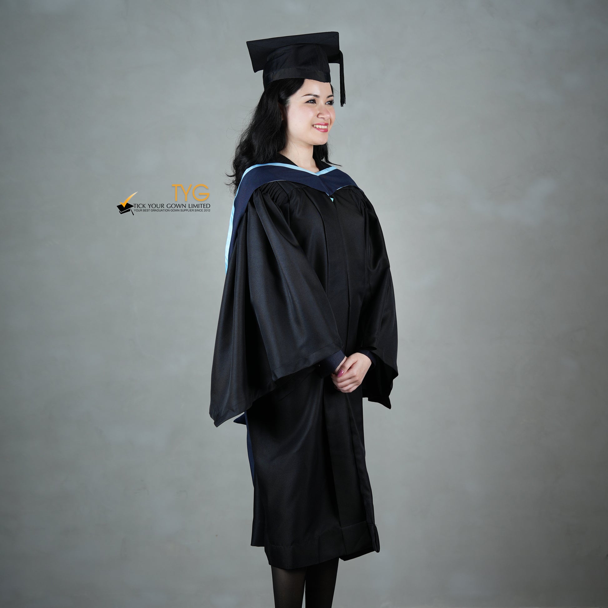 A profile view of a graduate in a black cap and gown with a navy blue hood with light blue lining against a gray background