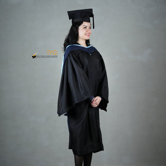 A profile view of a graduate in a black cap and gown with a navy blue hood with light blue lining against a gray background