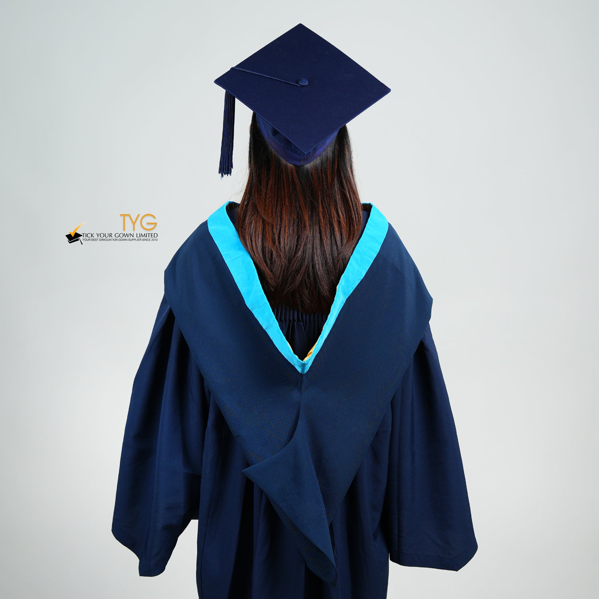 A back view of a person wearing a navy blue graduation gown and cap on a light gray background