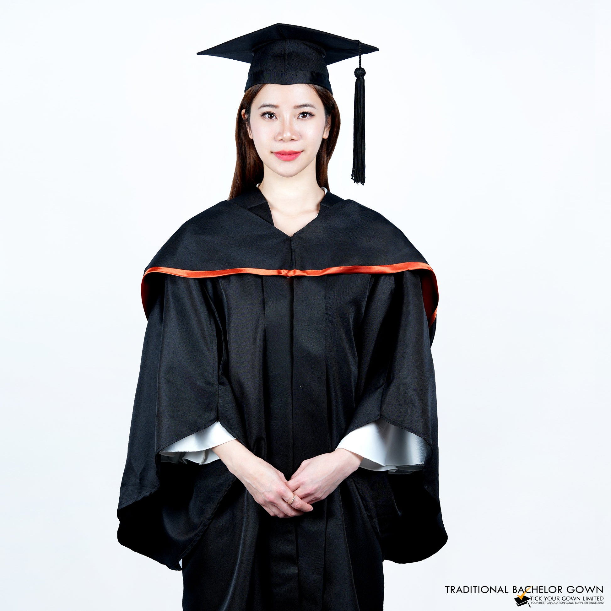 A person wearing a black bachelor graduation gown with a satin hood highlighted on the edge, and a mortarboard