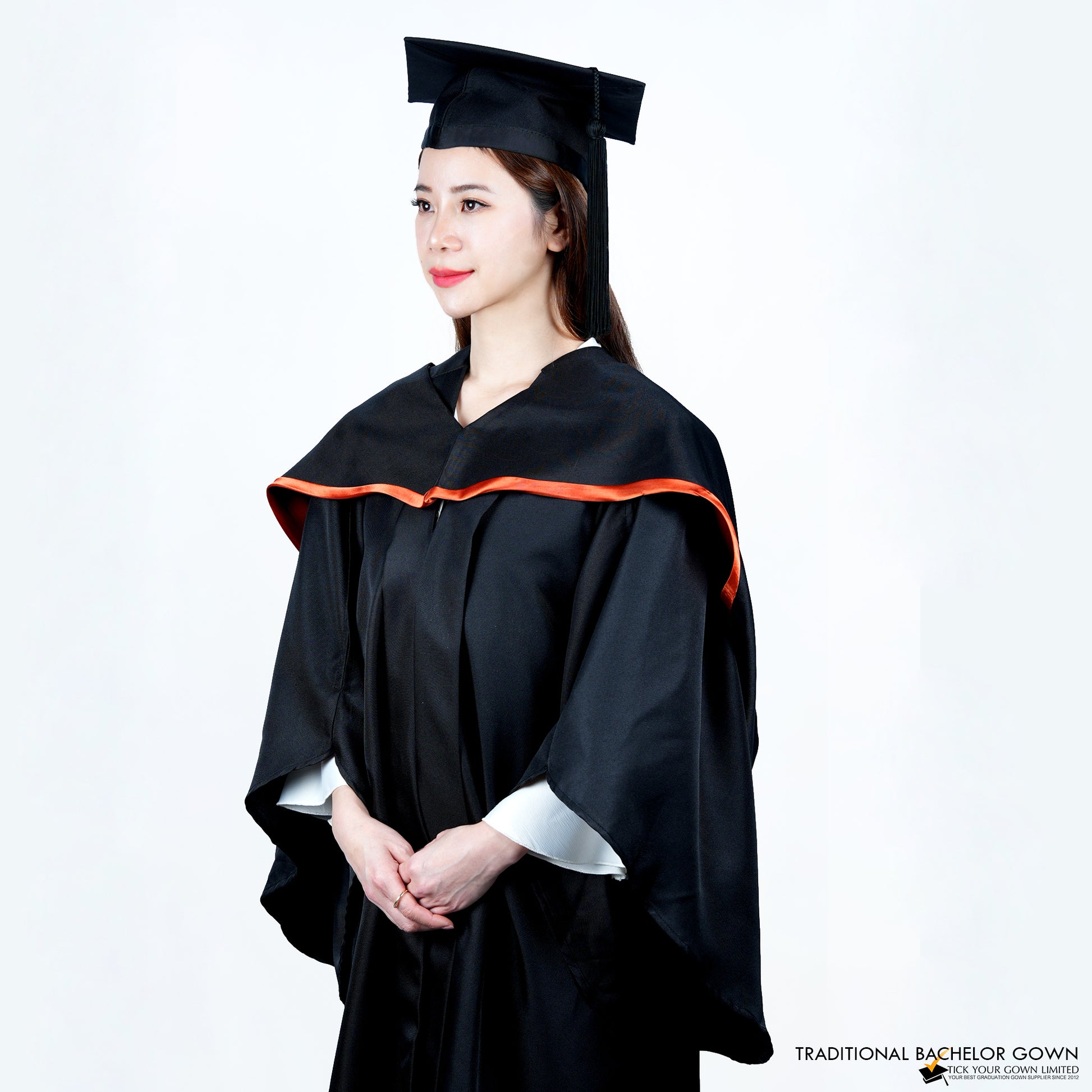 A person wearing a black bachelor graduation gown viewed from a front-side angle with a highlighted satin hood, and a mortarboard