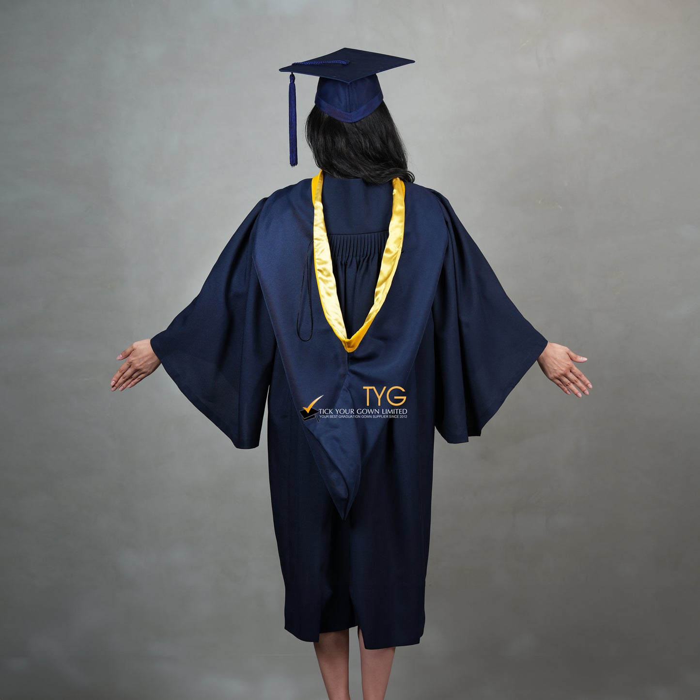 A full back view of a graduate in a navy cap and gown with a yellow hood against a gray background