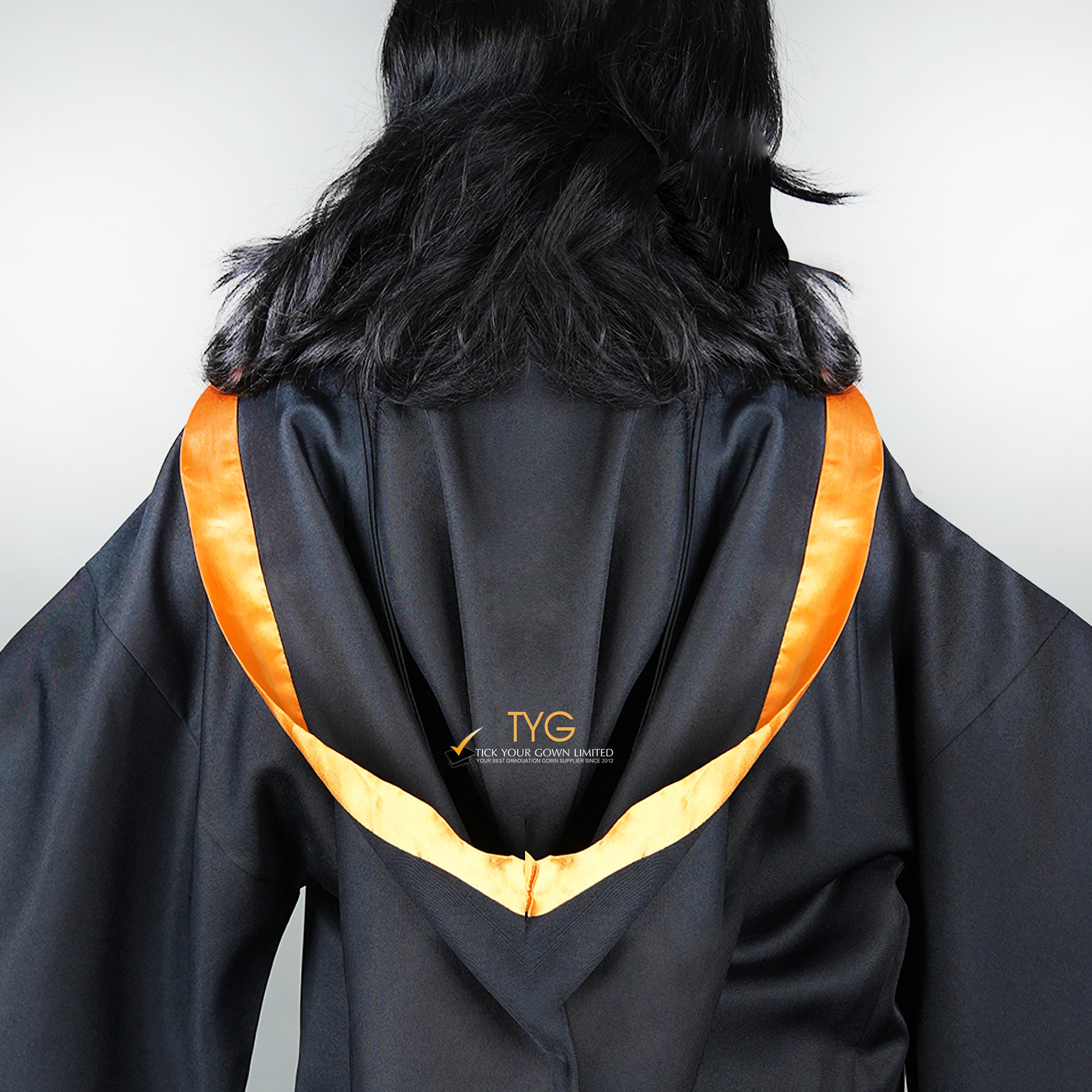 Detailed back view of a graduate in black graduation gown with an orange bachelor hood against a plain background