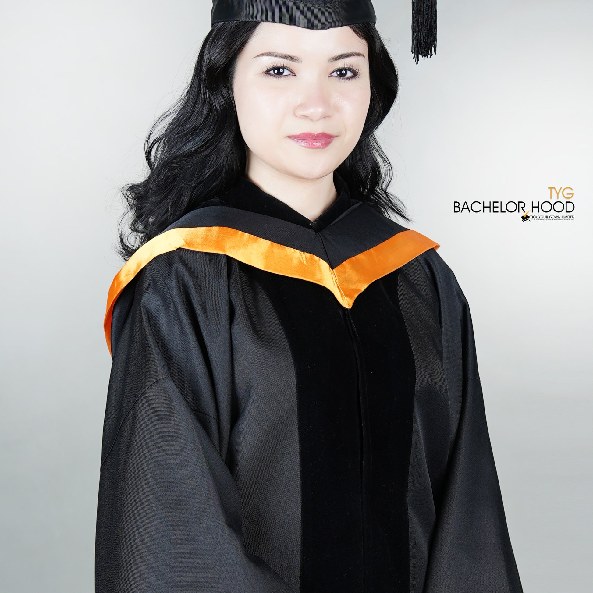 Graduate in black graduation gown with an orange bachelor hood against a plain background