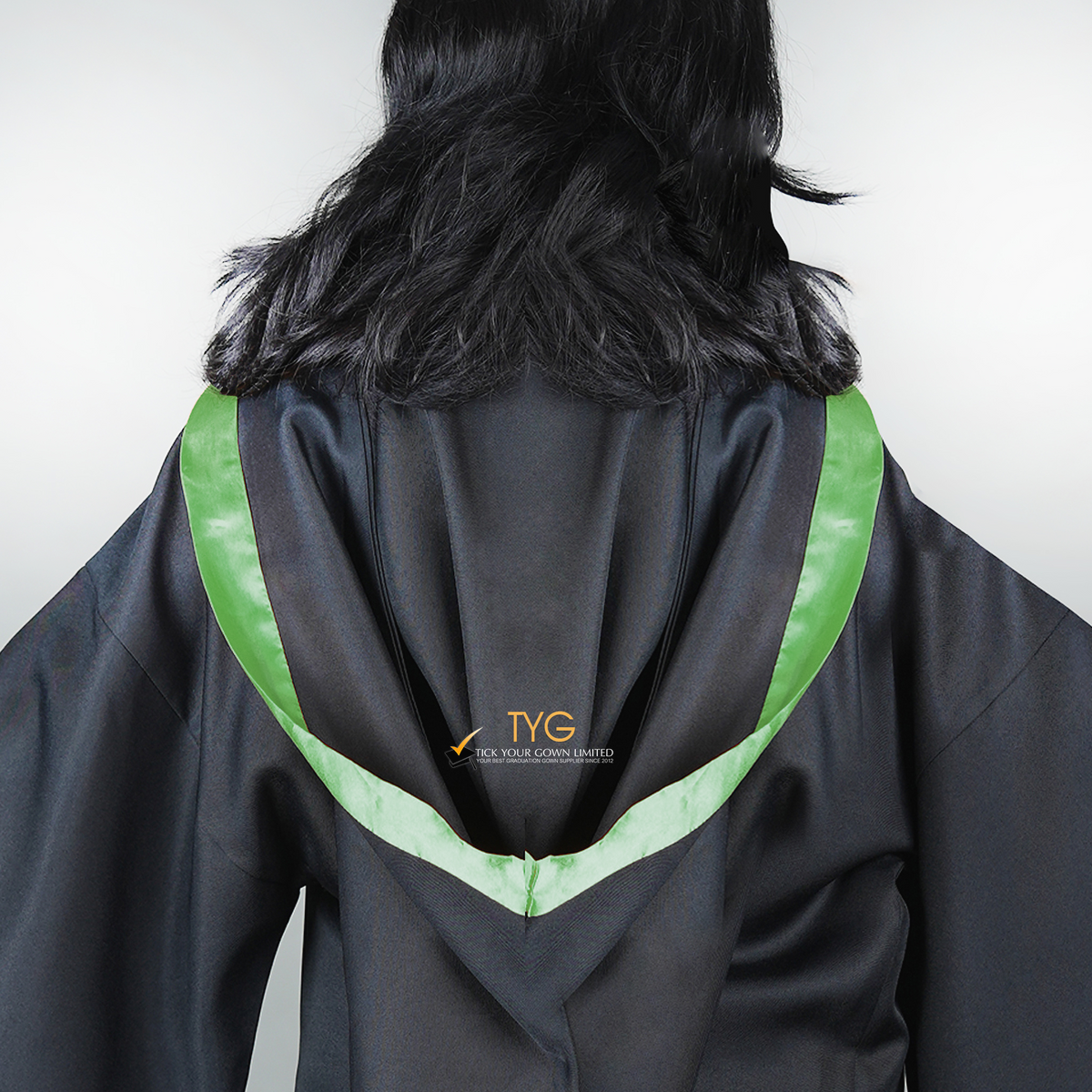 Detailed back view of a graduate in black graduation gown with a green bachelor hood against a plain background