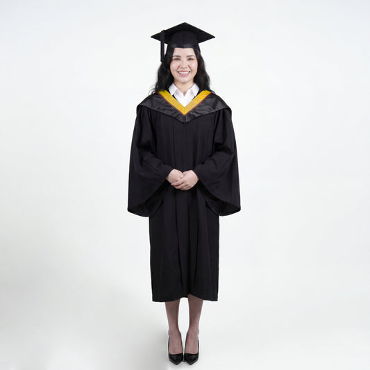 A woman wearing a black graduation gown and matching mortarboard cap stands against a light gray studio background.

The gown has a wide collar with gold and brown trim accent hood, and the model is posed with hands clasped in front.