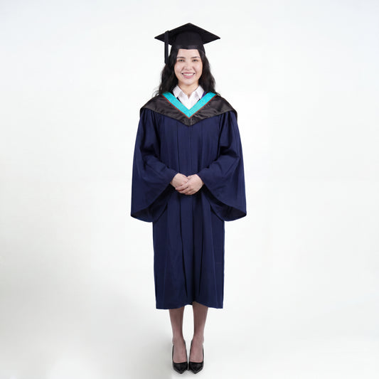A woman wearing a black graduation gown and matching mortarboard cap stands against a light gray studio background.

The gown has a wide collar with light blue and brown trim accent hood, and the model is posed with hands clasped in front.