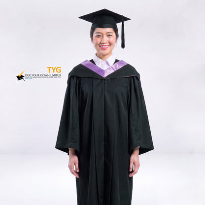 A woman wearing a black graduation gown and a black mortarboard cap stands against a light gray studio background. 

The gown has a lilac bachelor hood, and a white collared shirt is visible underneath.