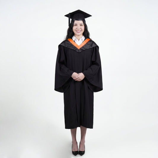 A woman wearing a black graduation gown and matching mortarboard cap stands against a light gray studio background.

The gown has a wide collar with orange and brown trim accent hood, and the model is posed with hands clasped in front.