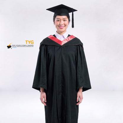 A woman wearing a black graduation gown and a black mortarboard cap stands against a light gray studio background. 

The gown has a red bachelor hood, and a white collared shirt is visible underneath.