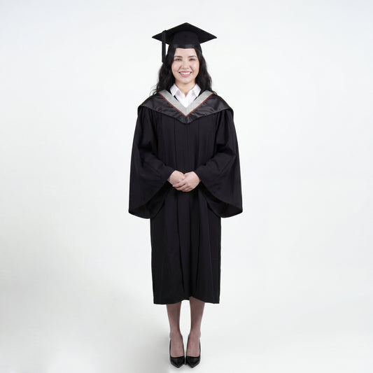 A woman wearing a black graduation gown and matching mortarboard cap stands against a light gray studio background.

The gown has a wide collar with silver and brown trim accent hood, and the model is posed with hands clasped in front.