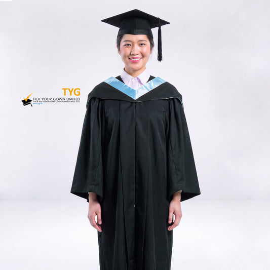 A woman wearing a black graduation gown and a black mortarboard cap stands against a light gray studio background. 

The gown has a sky blue bachelor hood, and a white collared shirt is visible underneath.