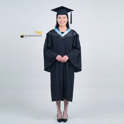 A woman wearing a black graduation gown and matching mortarboard cap stands against a light gray studio background.

The gown has a wide collar with light blue and brown trim accent hood, and the model is posed with hands clasped in front.