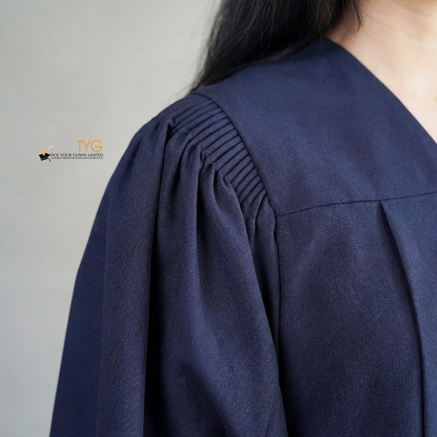 A detailed view of the pleated shoulder design of a person wearing a bachelors graduation gown in navy blue