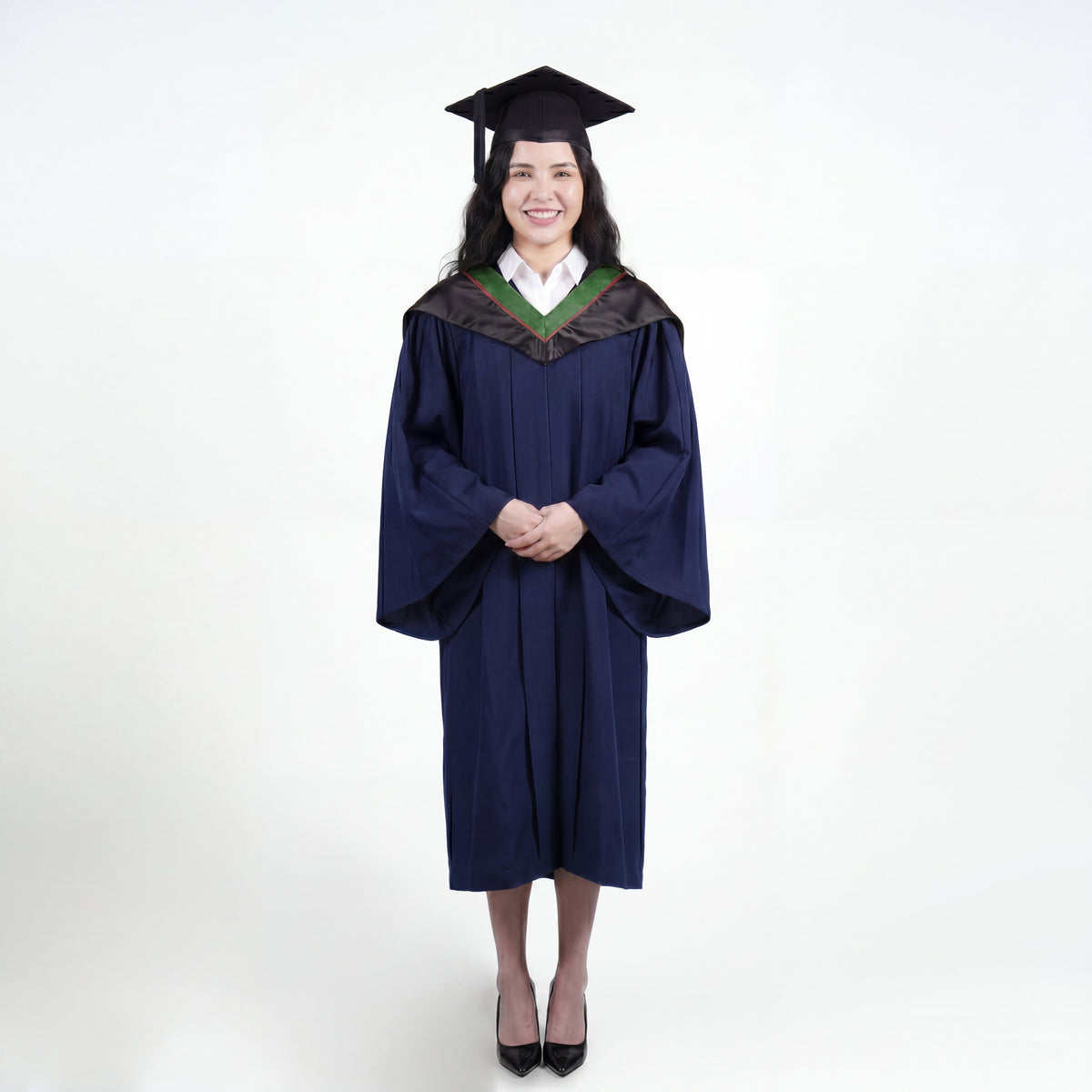 A woman wearing a navy blue graduation gown and matching mortarboard cap stands against a light gray studio background.

The gown has a wide collar with green and brown trim accent hood, and the model is posed with hands clasped in front.