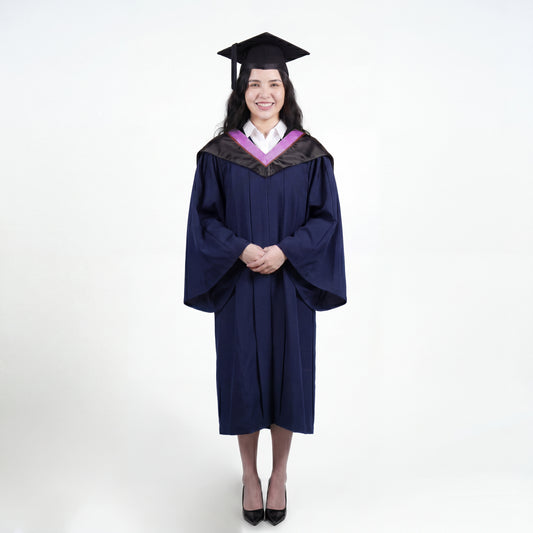 A woman wearing a navy blue graduation gown and matching mortarboard cap stands against a light gray studio background.

The gown has a wide collar with pink and brown trim accent hood, and the model is posed with hands clasped in front.