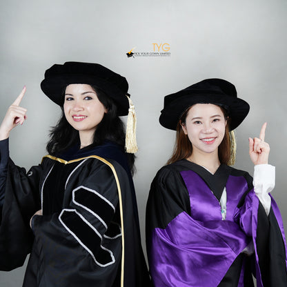 Two individuals in academic regalia pointing upwards against a gray background showcasing the doctoral bonnets