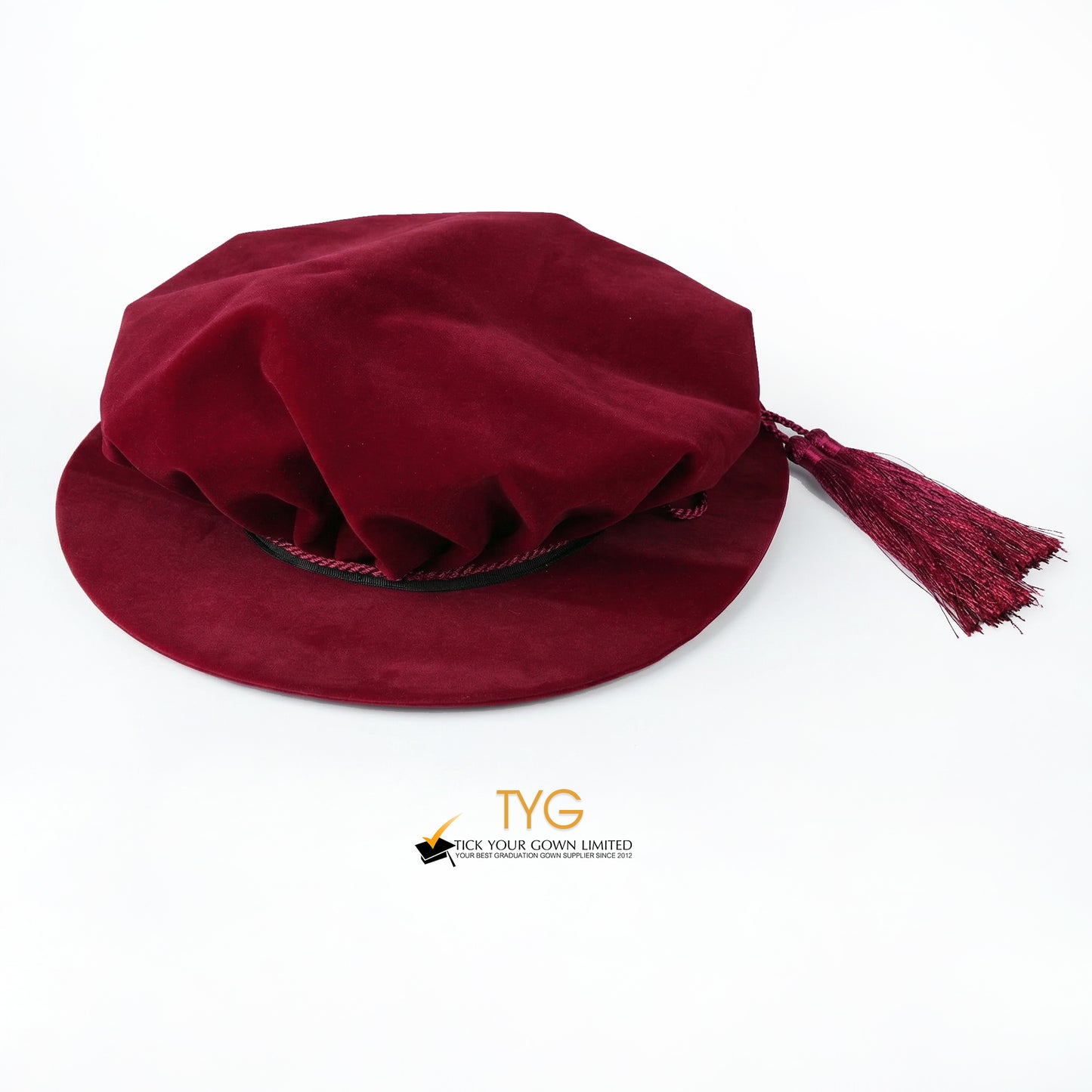 Front view of a maroon velvet doctoral bonnet with a soft gathered crown, black rim trim, and attached matching tassels extending to the right against a plain white background.