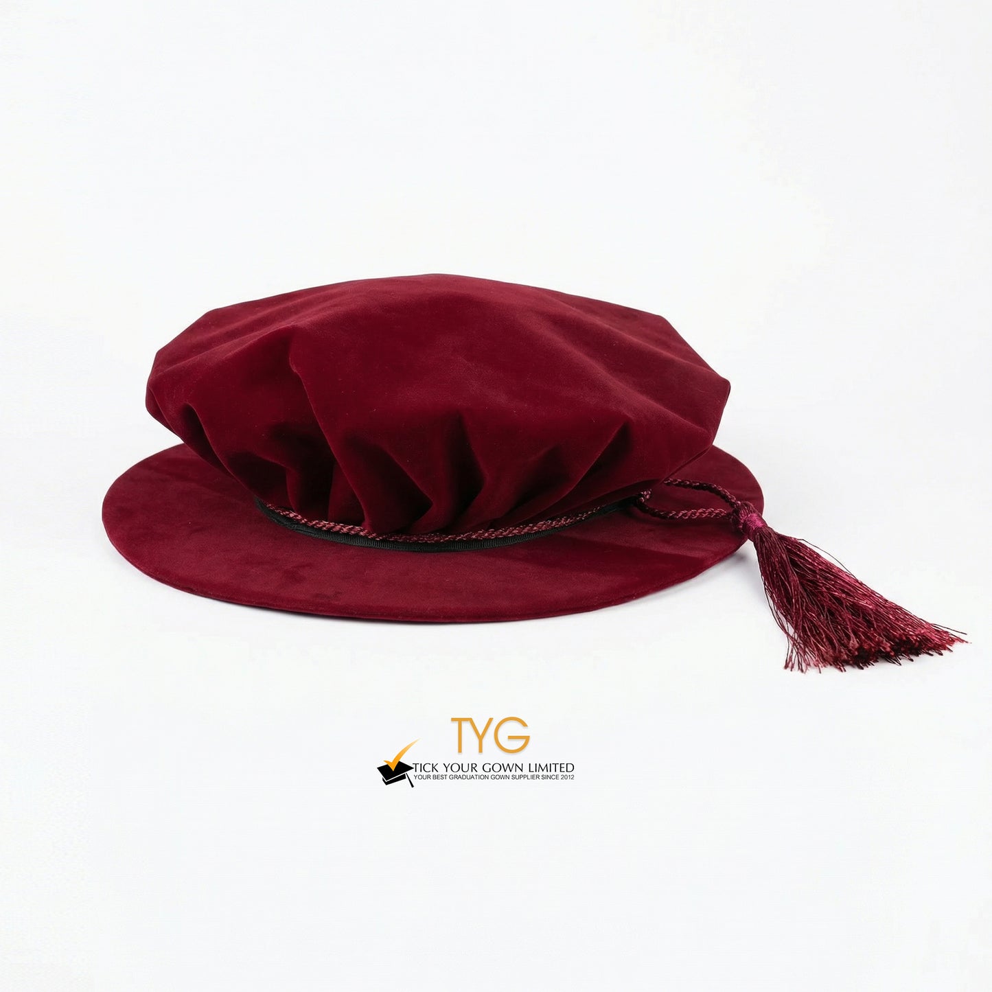 Eye-level front view of a maroon velvet doctoral bonnet showing its soft pleated crown, dark trim, and a draped maroon tassel extending to the right against a plain white background.