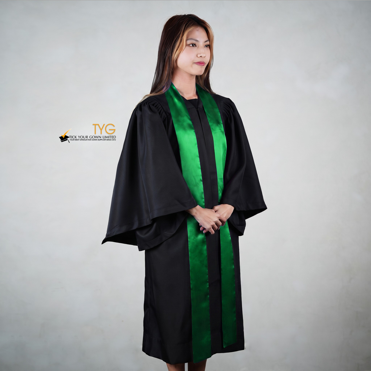 Profile view of a person wearing a black graduation gown with a green graduation sash on a gray background
