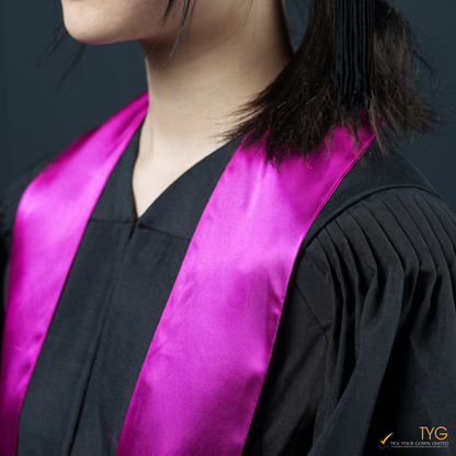 Person wearing a black graduation gown with a pink graduation sash on a dark background