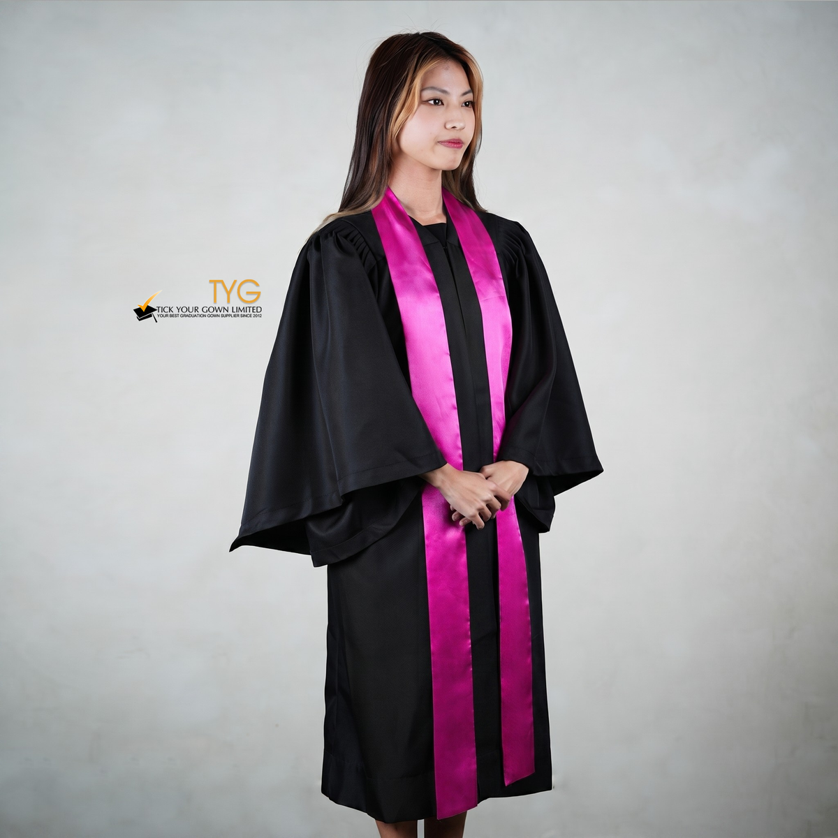 Profile view of a person wearing a black graduation gown with a pink graduation sash on a gray background