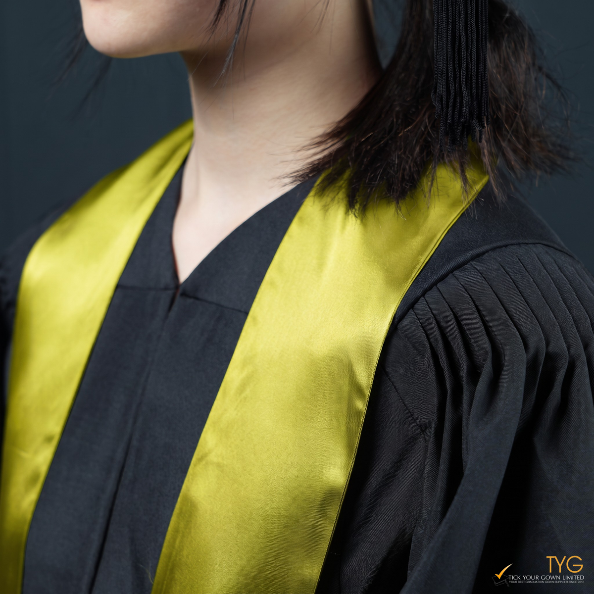 Person wearing a black graduation gown with a yellow graduation sash on a dark background