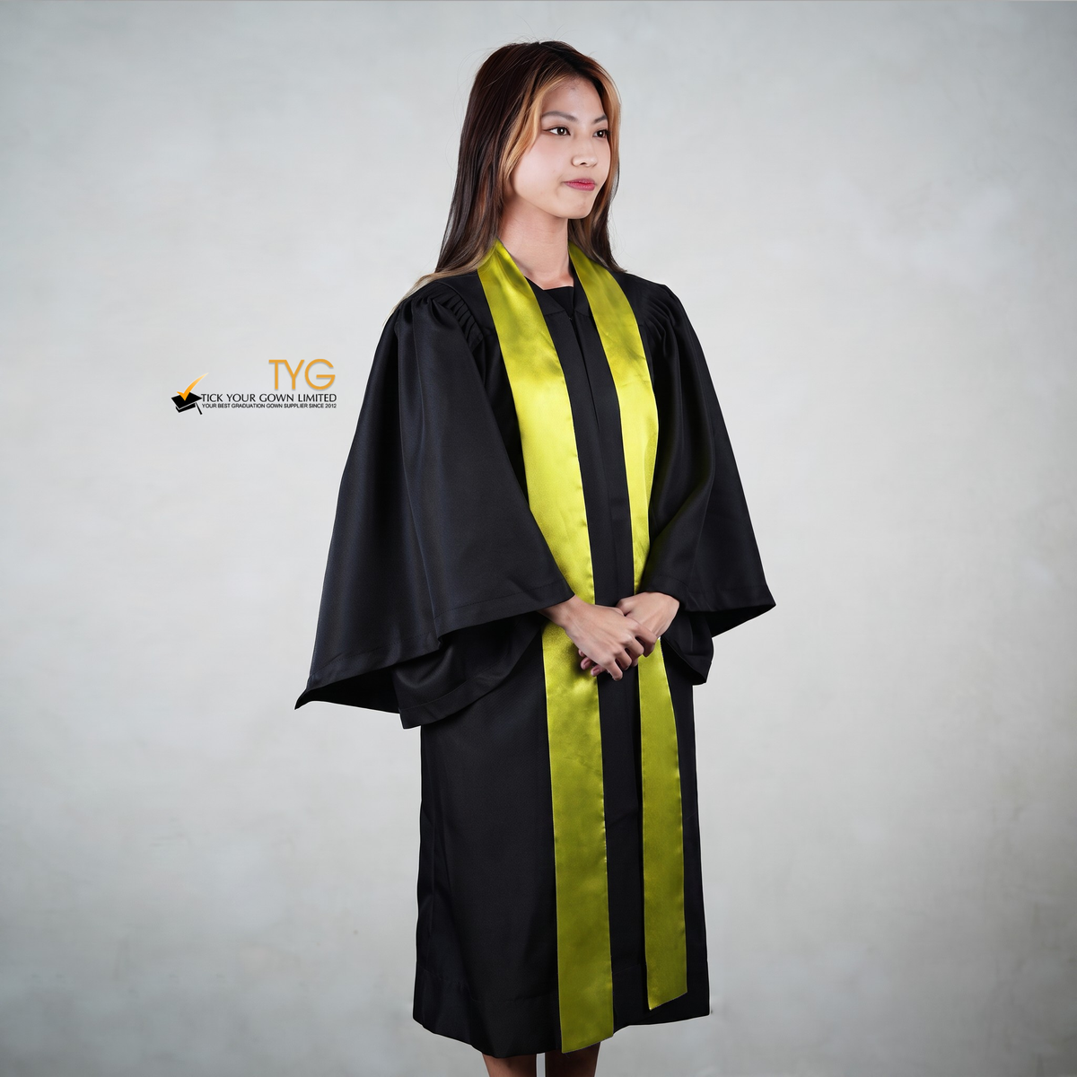 Profile view of a person wearing a black graduation gown with a yellow graduation sash on a gray background