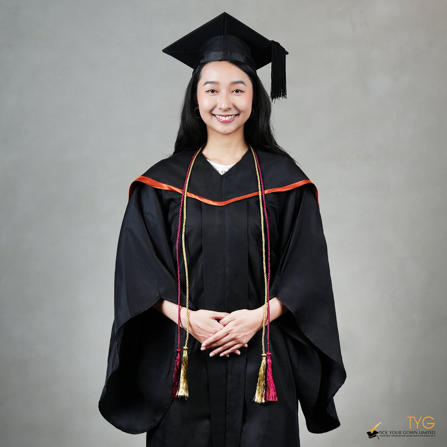 Graduate in black cap and gown with red and gold honour cords on a gray background