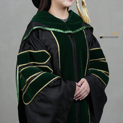 A detailed profile view of a person wearing a PhD graduation gown in black with forest green velvet panels, matching sleeve bars, gold trim, and a matching doctoral bonnet with gold tassel.