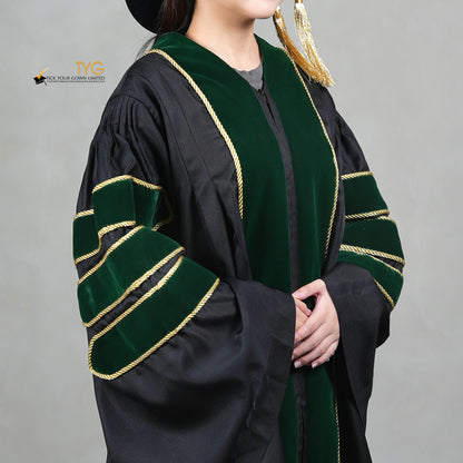 A detailed profile view of a person wearing a PhD graduation gown in black with forest green velvet panels, matching sleeve bars, gold trim, and a matching doctoral bonnet with gold tassel.