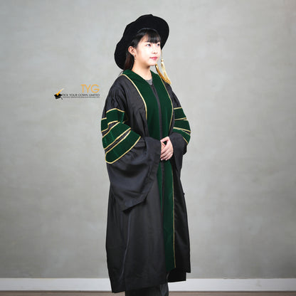 A profile view of a person wearing a PhD graduation gown in black with forest green velvet panels, matching sleeve bars, gold trim, and a matching doctoral bonnet with gold tassel.