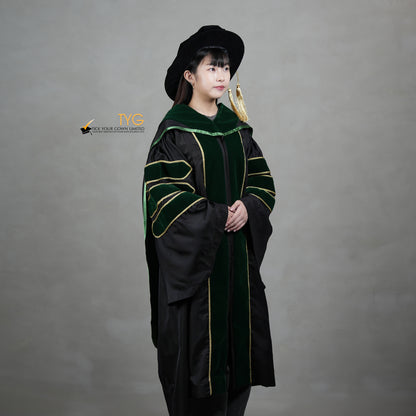 A profile view of a person wearing a PhD graduation gown in black with forest green velvet panels, matching sleeve bars, gold trim, and a matching doctoral bonnet with gold tassel.