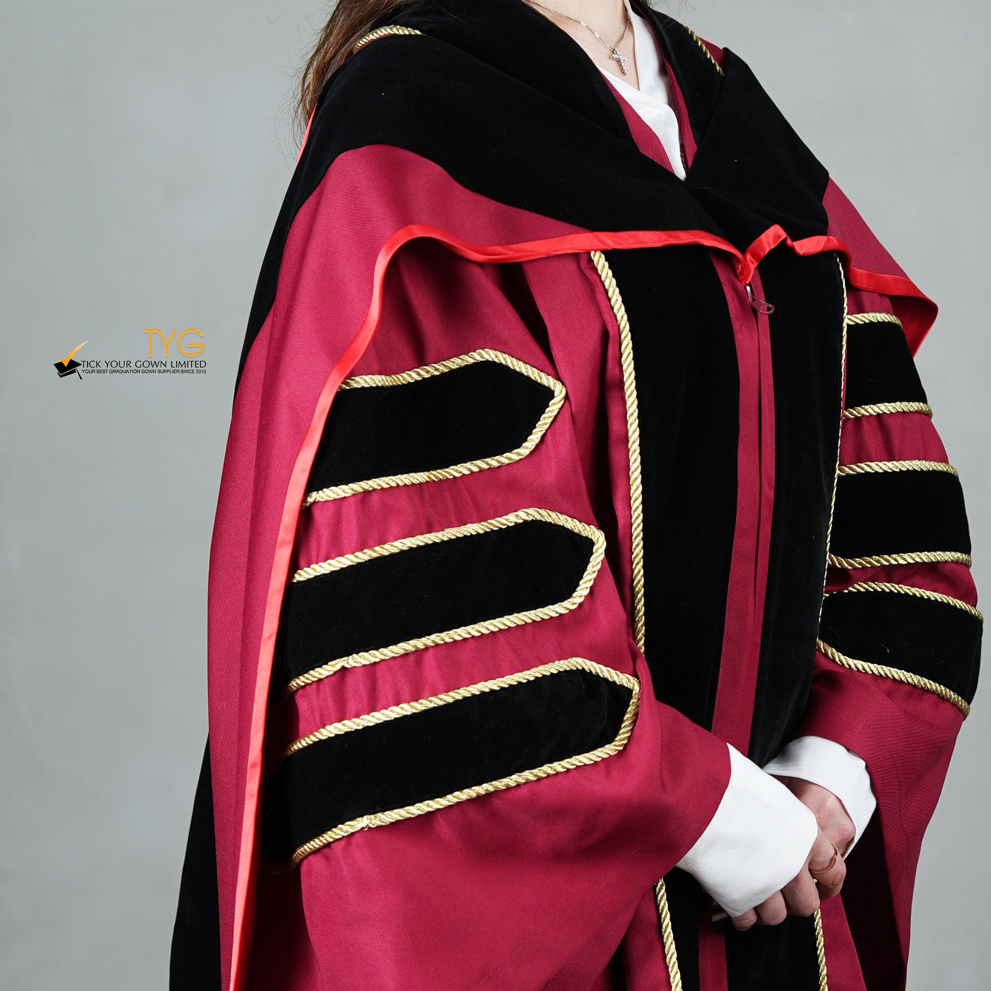 A detailed profile view of a person wearing a doctoral graduation gown in maroon with black velvet panels, matching black velvet sleeve bars in gold trim