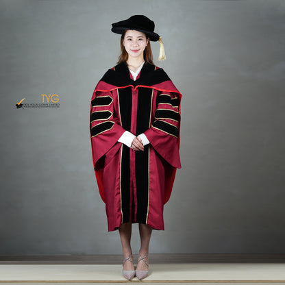 A front view of a person wearing a doctoral graduation gown in maroon with black velvet panels, matching black velvet sleeve bars, gold trim, and a black doctoral bonnet with gold tassel.