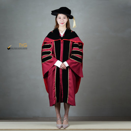 A front view of a person wearing a doctoral graduation gown in maroon with black velvet panels, matching black velvet sleeve bars, gold trim, and a black doctoral bonnet with gold tassel.