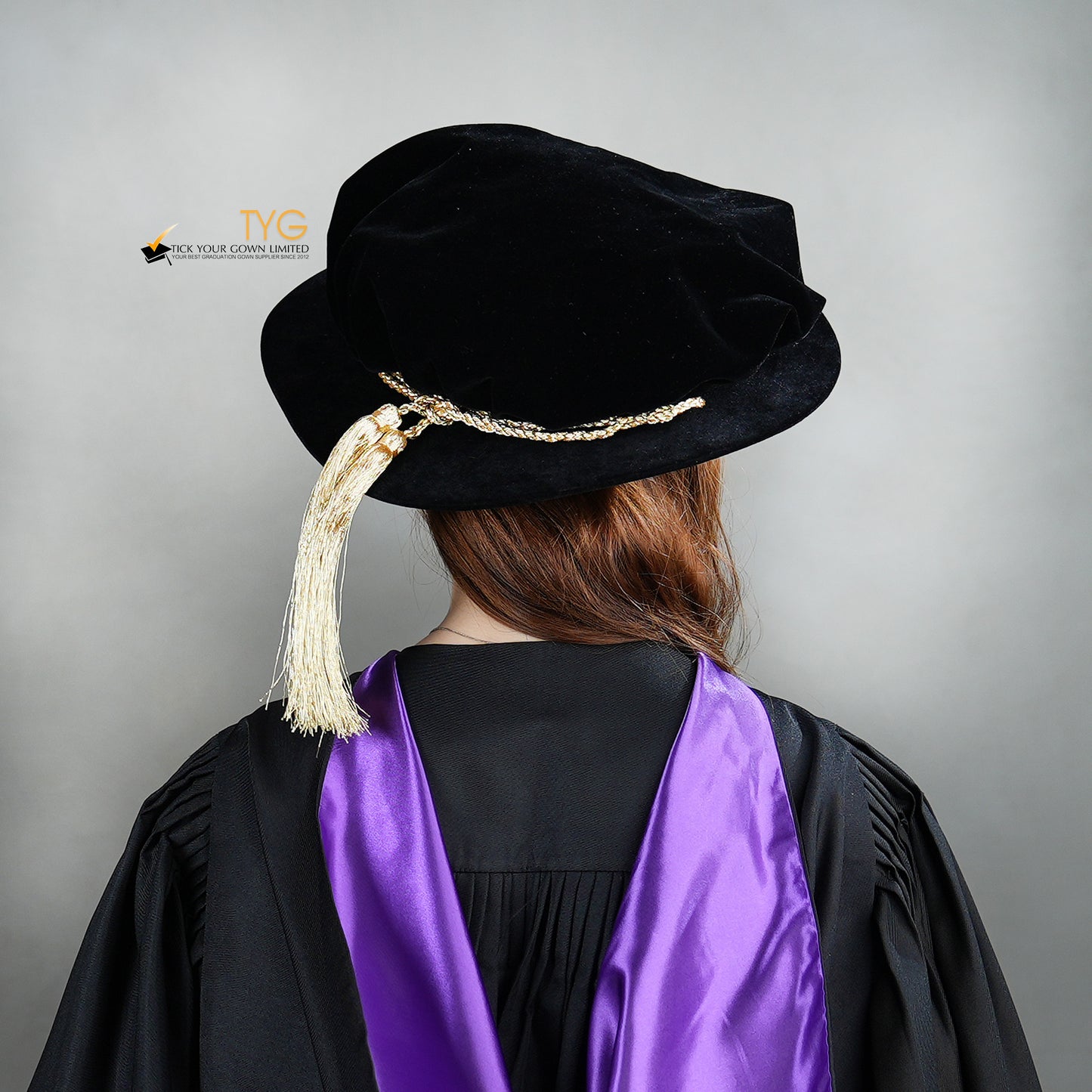 Back view of a person wearing a black doctoral bonnet and purple gown with a gold tassel on a gray background