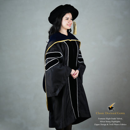 A profile view of a person wearing a PhD classic black velvet graduation gown with silver sleeve bars, silver front trim, and a black doctoral bonnet with gold tassel.