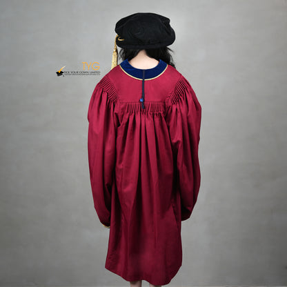 A back view of a person wearing a premium honorary graduation gown in maroon with royal blue velvet panels, gold trim, and a matching doctoral bonnet with gold tassel.