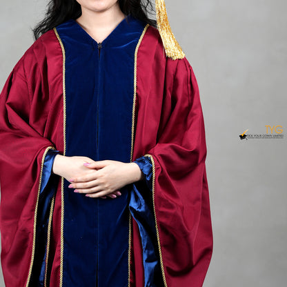 A detailed view of a person wearing a premium honorary graduation gown in maroon with royal blue velvet panels, gold trim, and a matching doctoral bonnet with gold tassel.