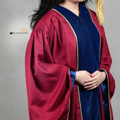 A detailed profile view of a person wearing a premium honorary graduation gown in maroon with royal blue velvet panels, gold trim, and a matching doctoral bonnet with gold tassel.