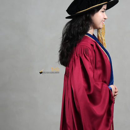 A detailed side view of a person wearing a premium honorary graduation gown in maroon with royal blue velvet panels, gold trim, and a matching doctoral bonnet with gold tassel.