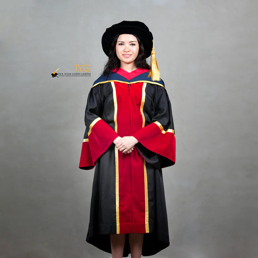 Front view of a person wearing a premium honorary graduation gown in black with red velvet panels, gold trim, matching red velvet sleeve cuffs, and a doctoral bonnet with gold tassel