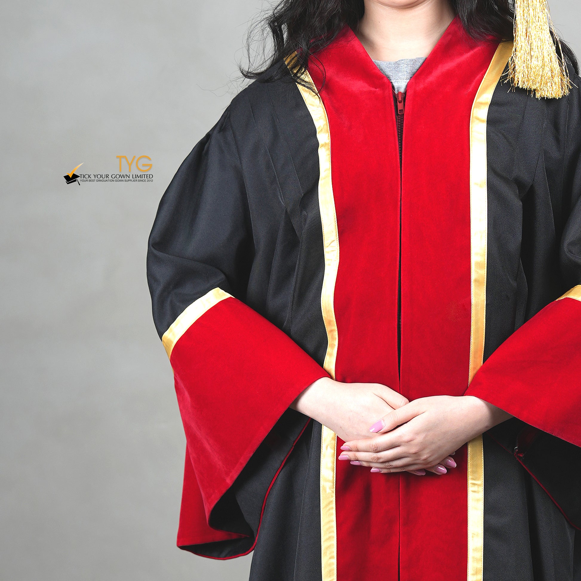 A close-up of a honorary gown in black with red velvet panels, gold trim, and matching red velvet bell sleeves